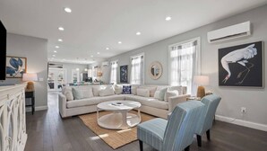 A spacious living room with a large L-shaped sofa, a round coffee table, and a dining area in the background.