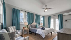 A bedroom with a bed, two chairs, a nightstand, a lamp, and a ceiling fan.
