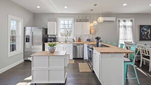 A modern kitchen with white cabinetry, a stainless steel refrigerator, a dishwasher, and a wooden island.