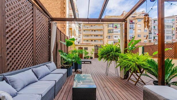 Une terrasse extérieure couverte, aménagée avec un canapé, une table et des plantes en pot.