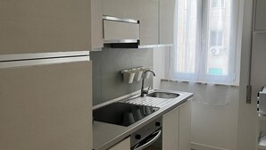 Et moderne køkken med indbygget ovn, stålvask og et vindue med lette gardiner.