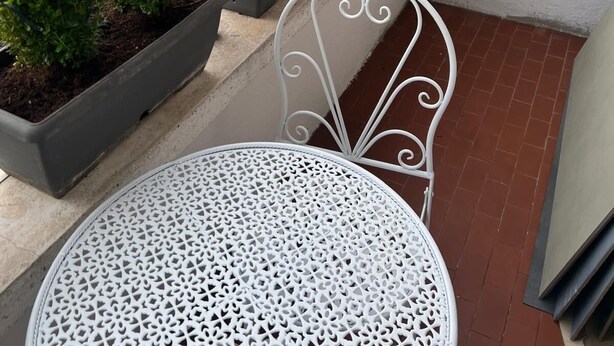 En balkon med en hvid metalstol og krukker med planter.