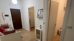 En moderne lejlighed med trægulv, en hvid sofa, en rød pude, en loftslampe og en dør til et andet rum.