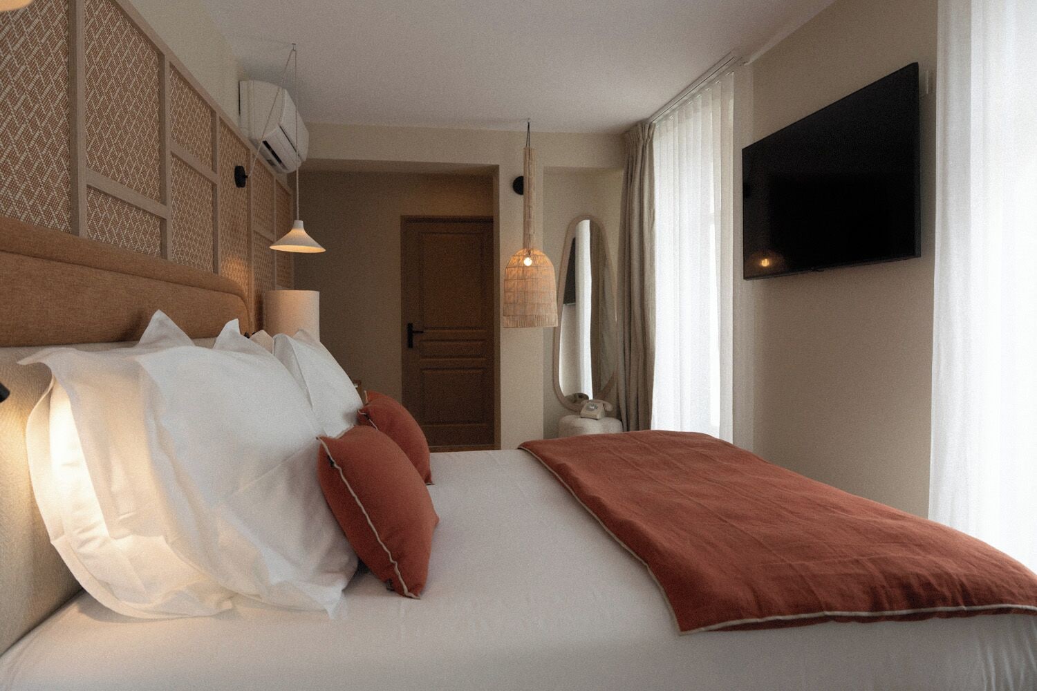 Una habitación de hotel con cama, almohadas, televisión y ventana con cortinas.
