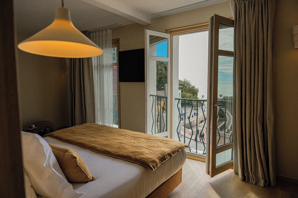A bedroom with a bed, a hanging lamp, a TV, and a balcony with a railing.