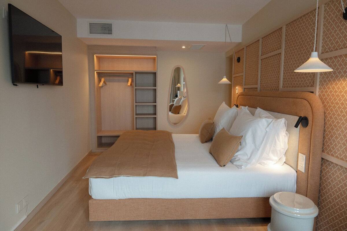A bedroom with a bed, a wardrobe, a mirror, and a television.