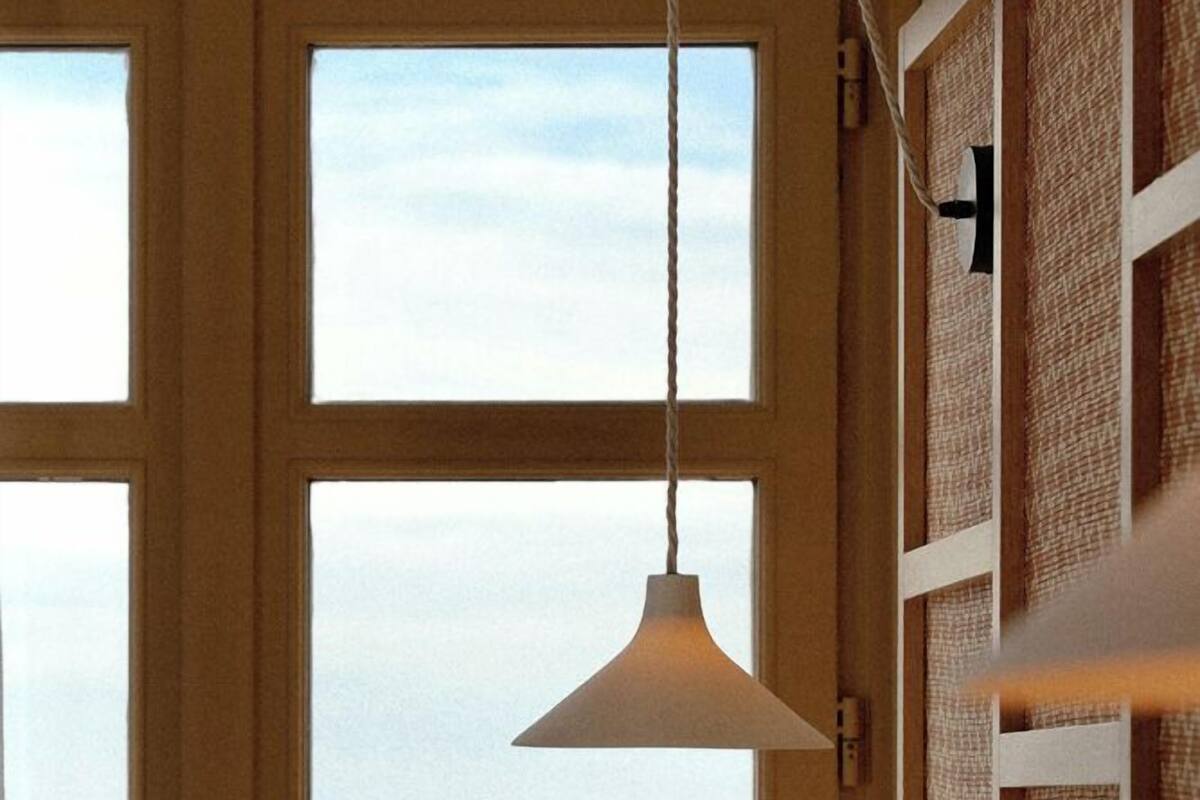 A room with a bed, a hanging light fixture, and a view of the ocean through a large window.