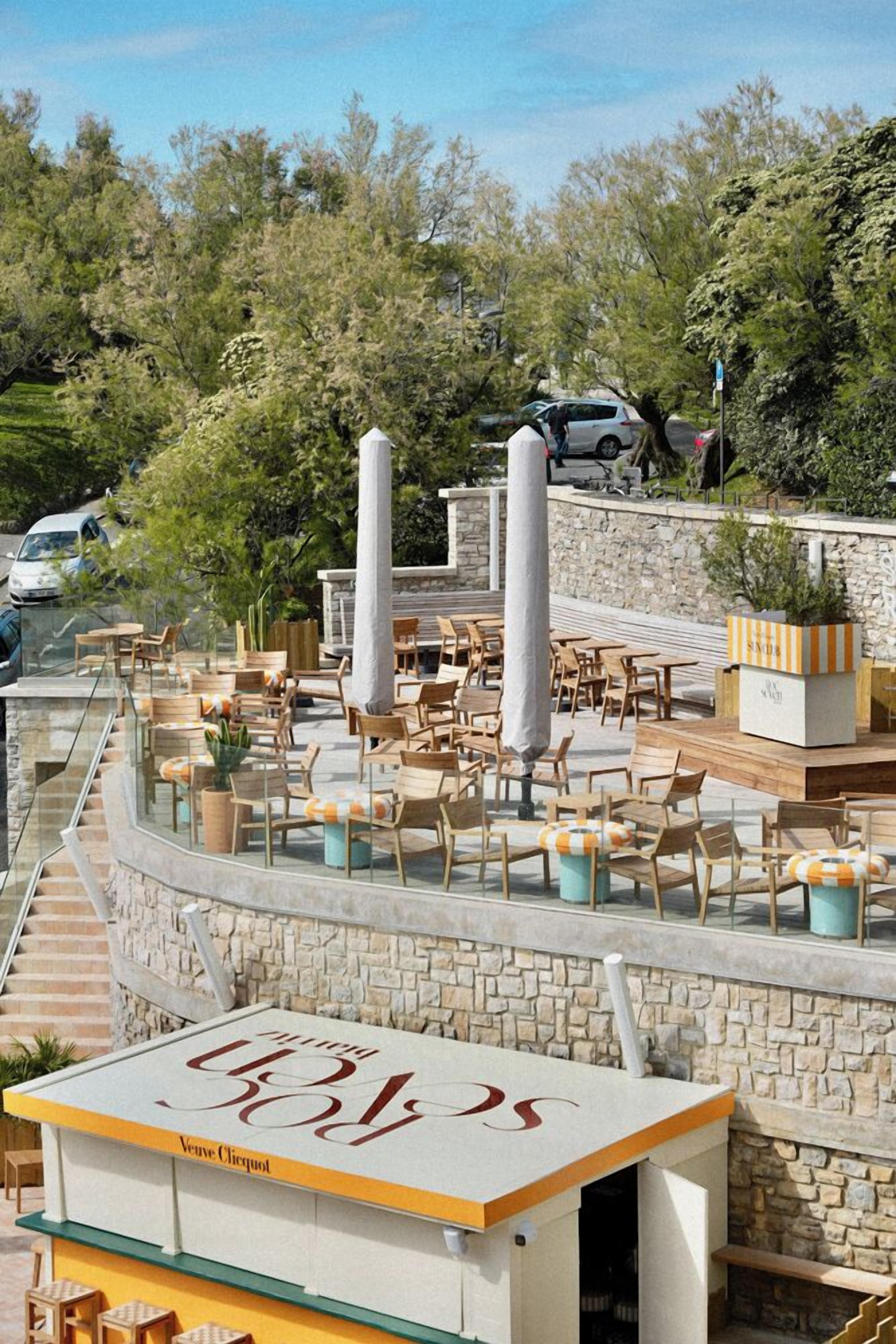 An outdoor seating area with wooden tables and chairs, stone walls, and a staircase leading up.