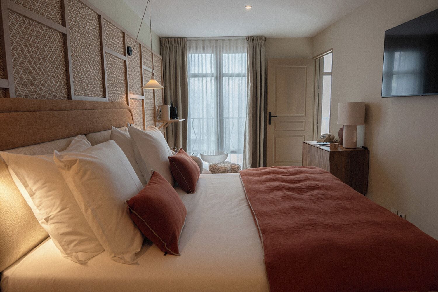 A hotel room with a large bed, a TV, and a window with curtains.