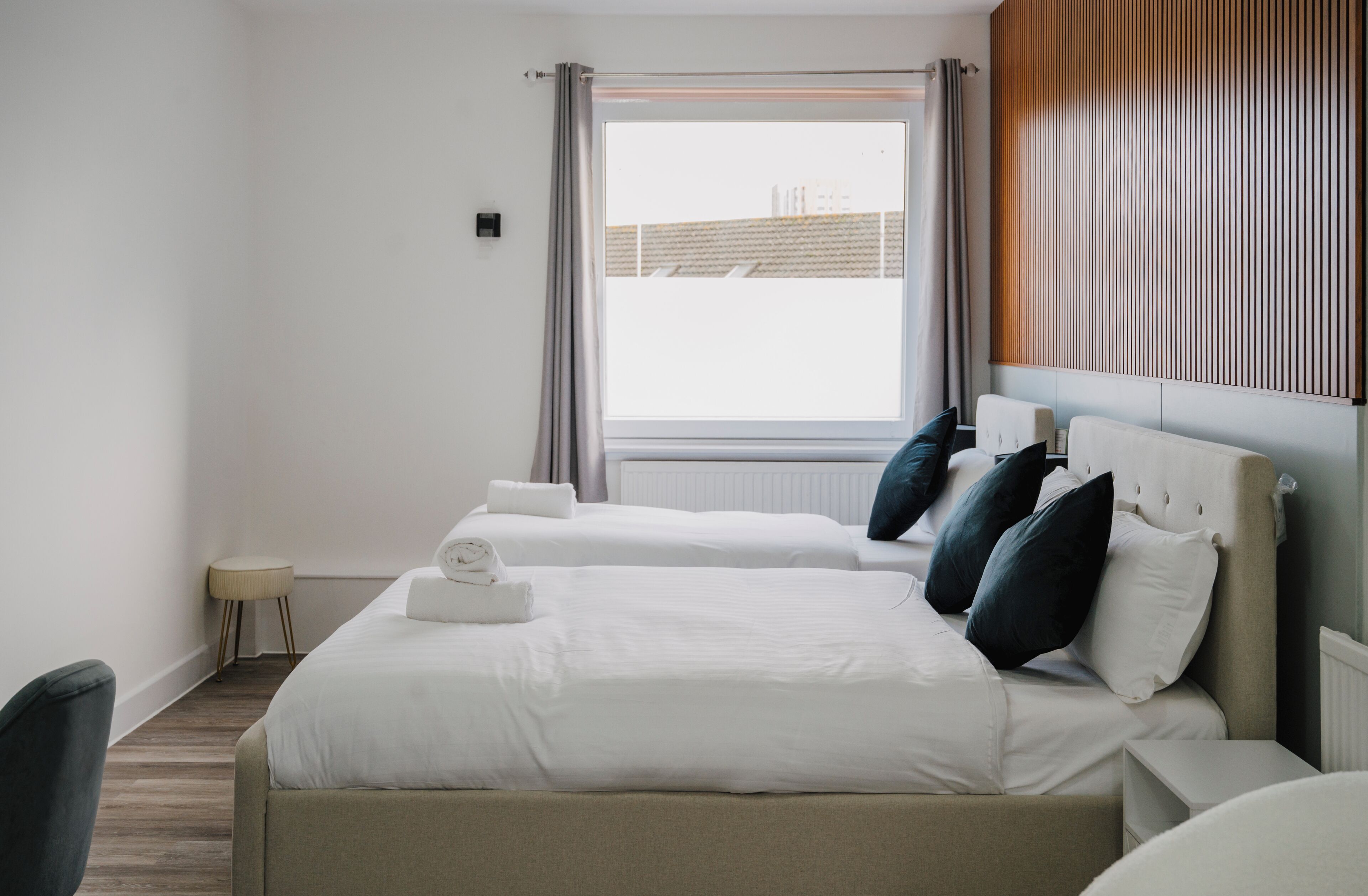 Ein Hotelzimmer mit zwei Betten, einem kleinen Beistelltisch, einem Sessel und einem Fenster mit Vorhängen.
