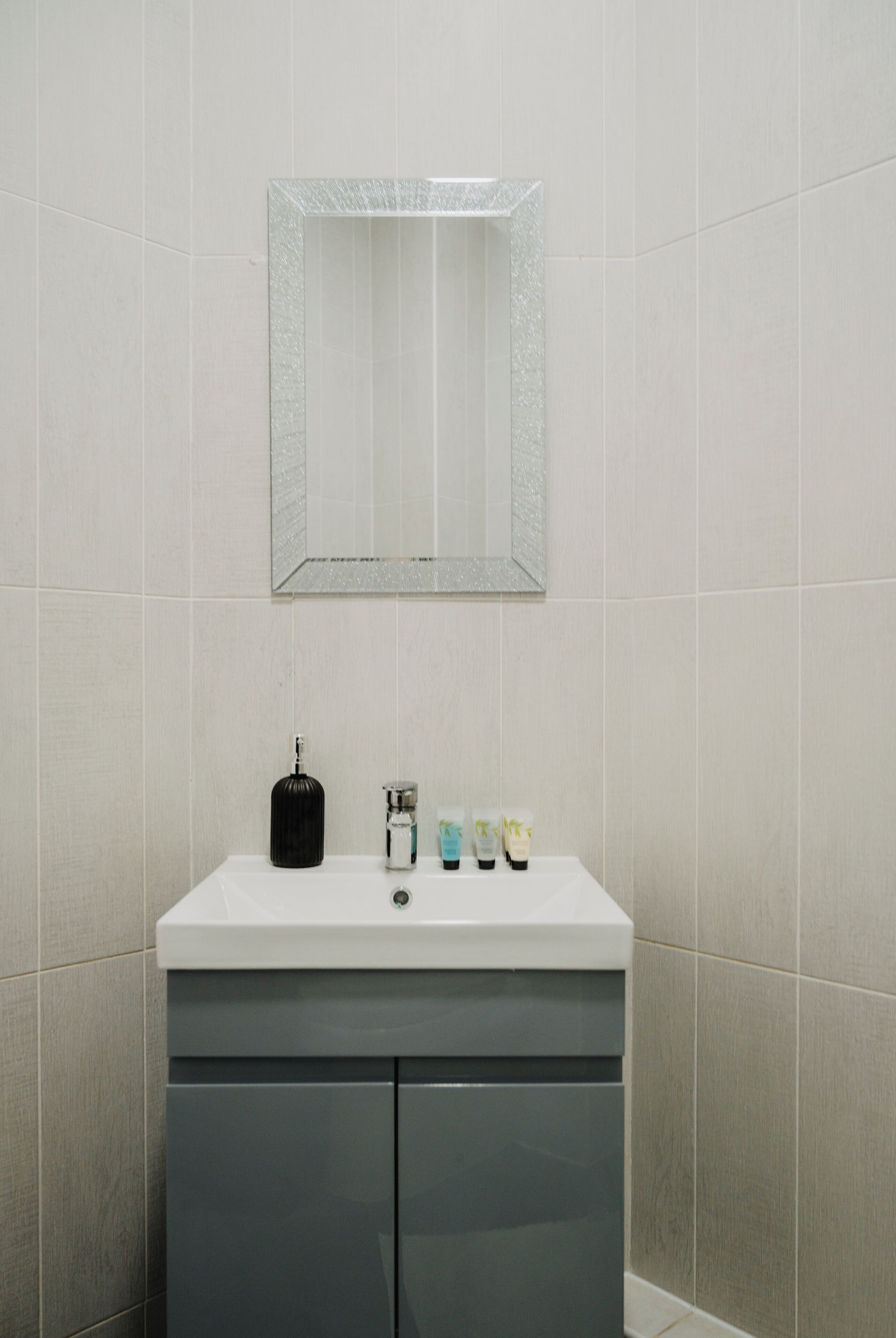 A bathroom with a white sink, a mirror, and toiletries on the counter.