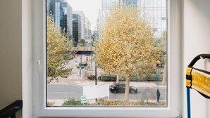 A view through a window of a cityscape with modern buildings, a tree, and a road with a car. - WNS Hotel (London)