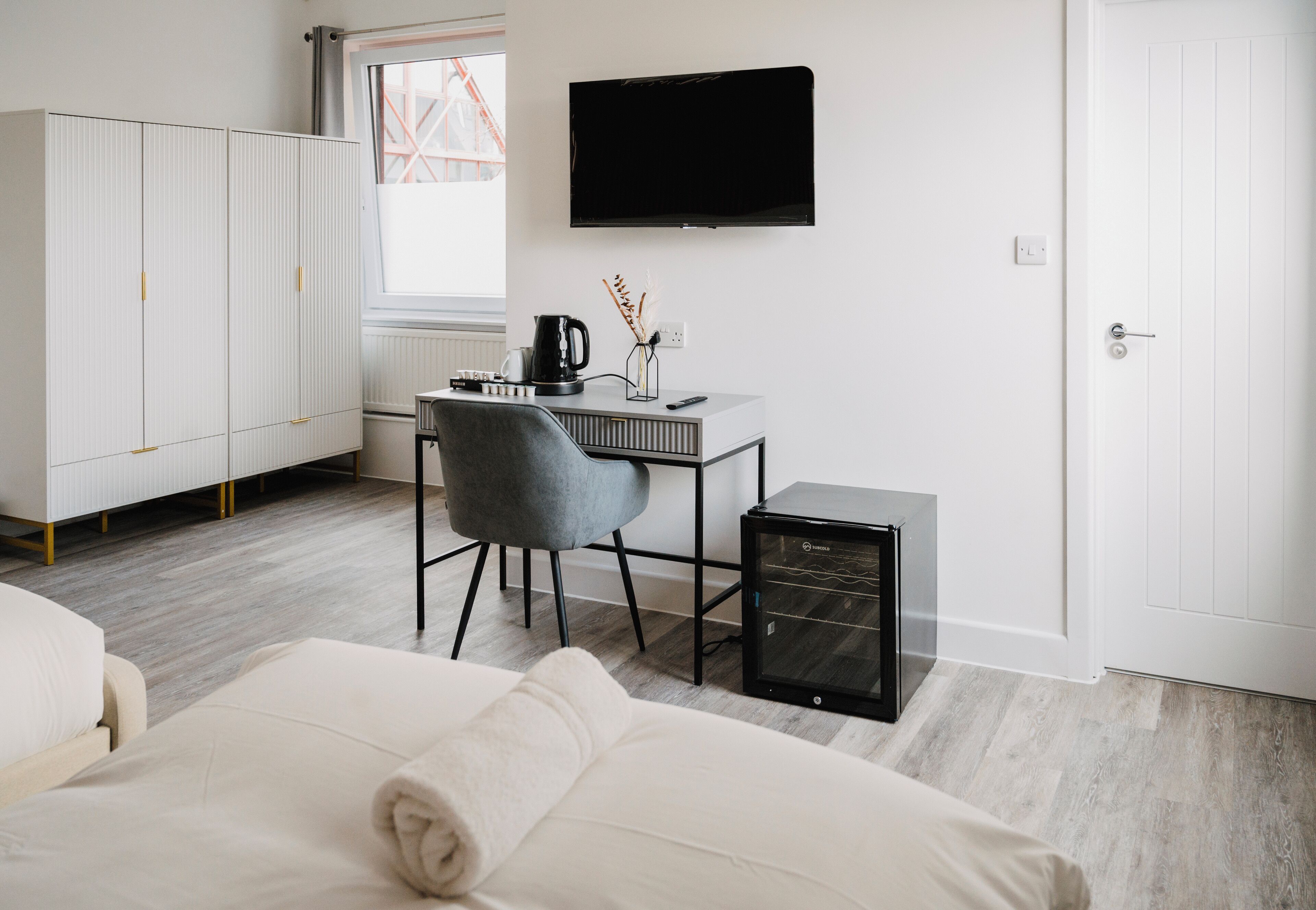 A modern hotel room with a bed, a desk with a chair, a television, and a wardrobe.