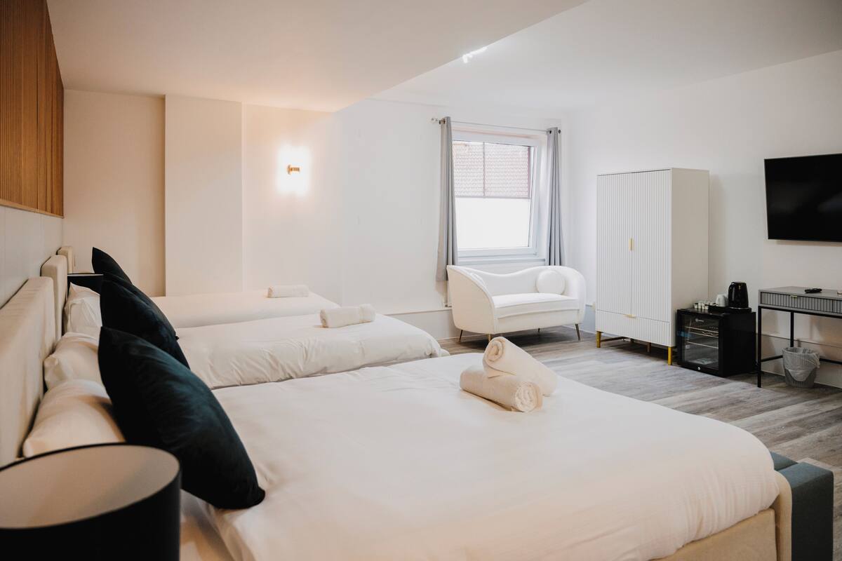 A modern hotel room with a large bed, a sitting area, a wardrobe, and a television.