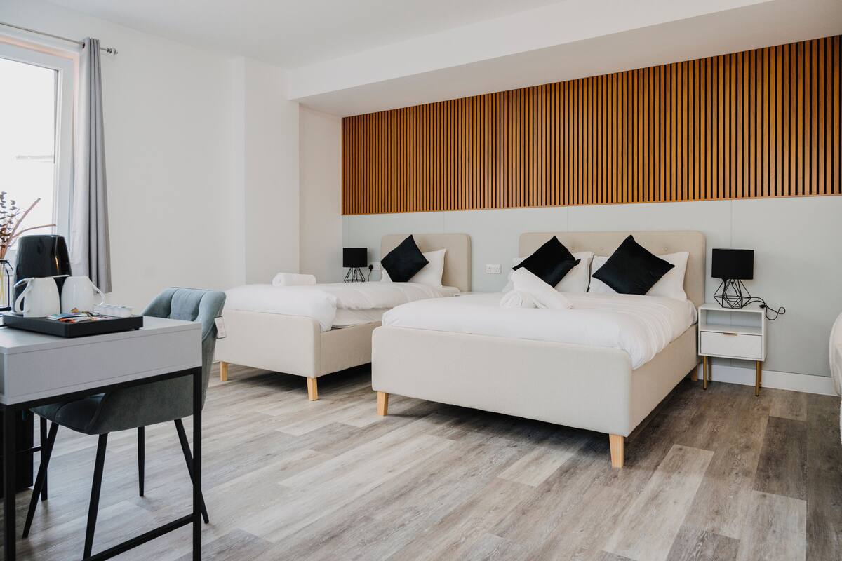 A modern hotel room with two beds, a desk, and a chair.
