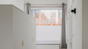 A narrow hallway with a radiator, a radiator cover, a window with curtains, and a radiator on the wall. - WNS Hotel (London)