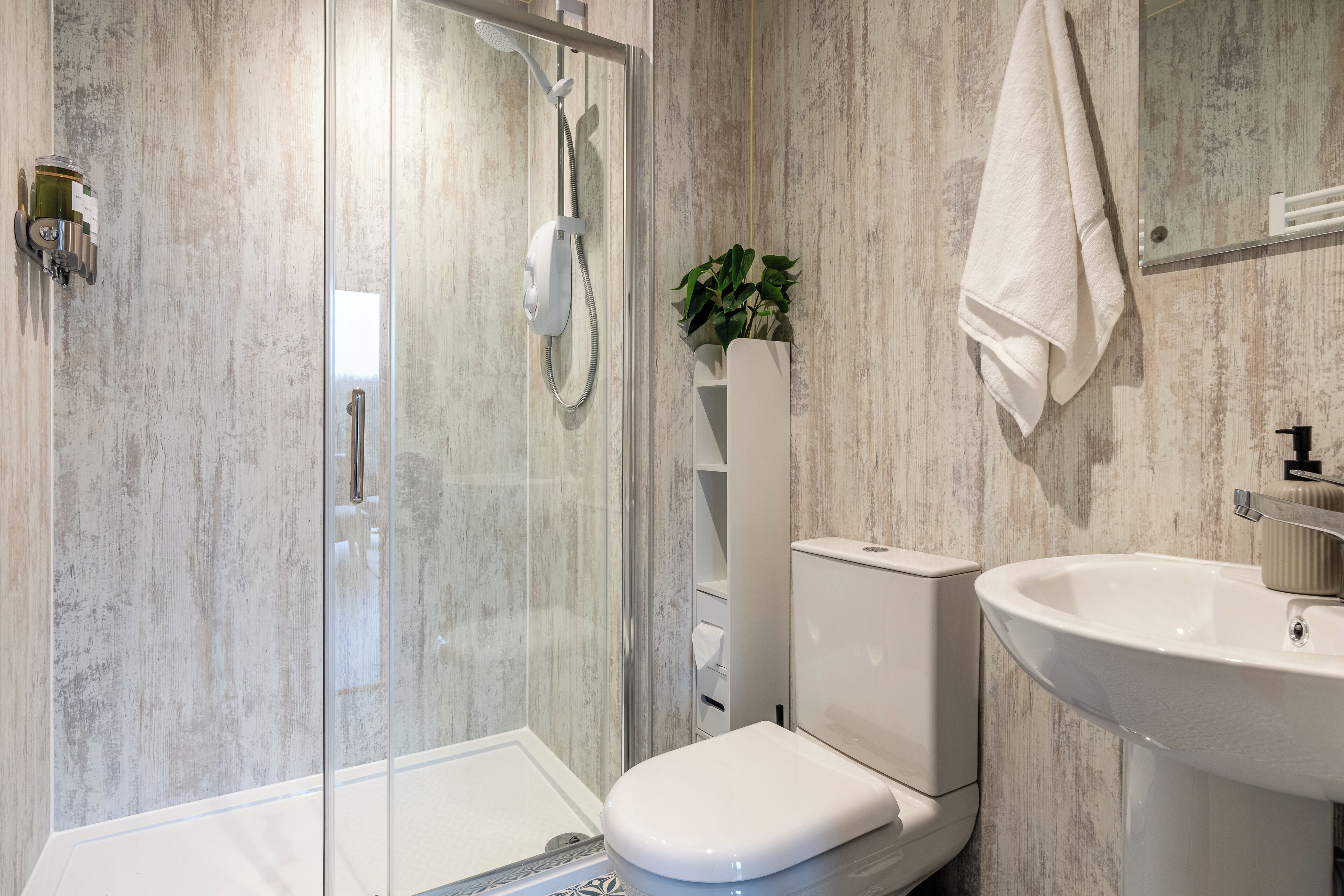 A modern bathroom with a glass shower enclosure, a white toilet, and a sink with a mirror above it.