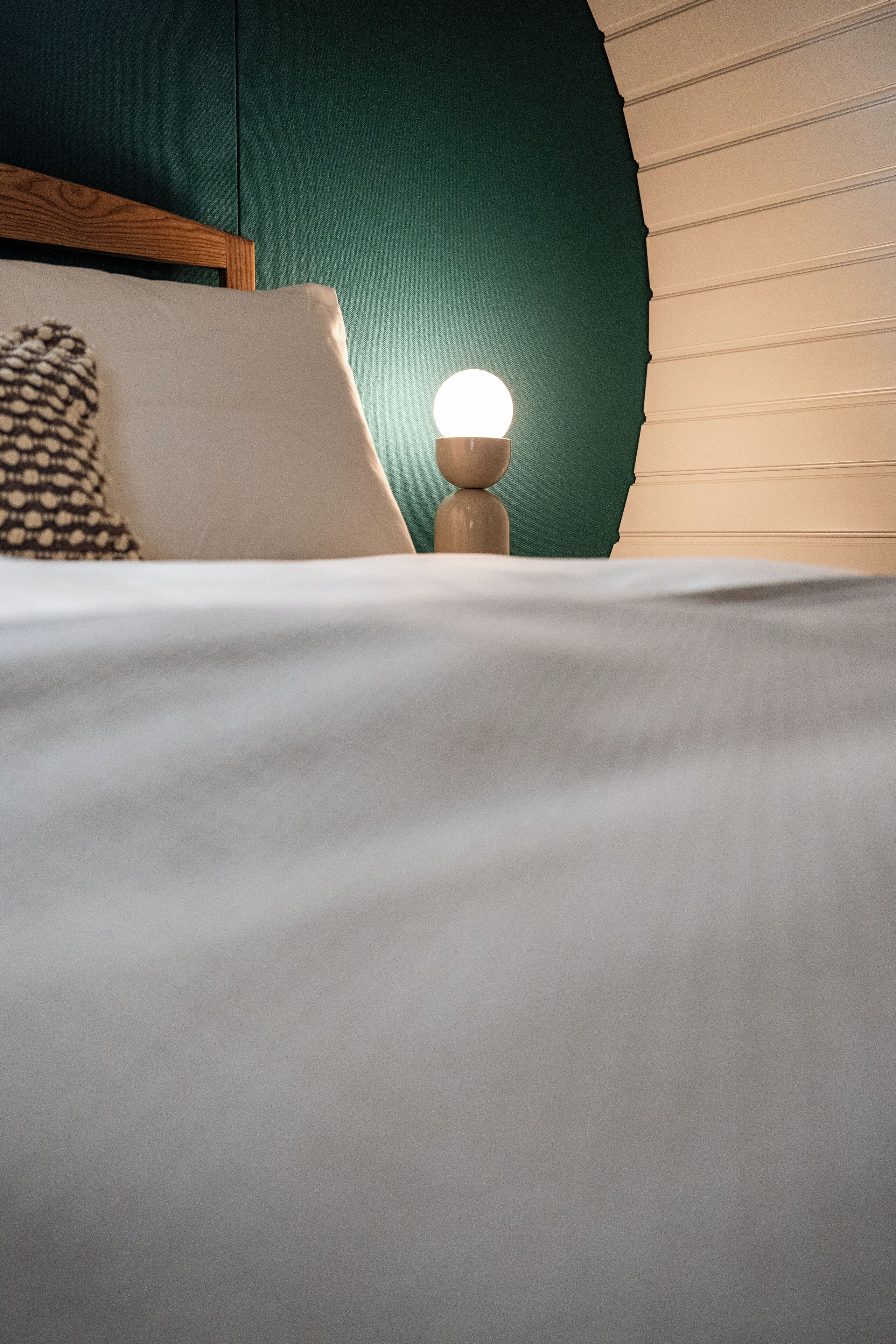 A neatly made bed with a white comforter and pillows, a bedside lamp, and a green wall.