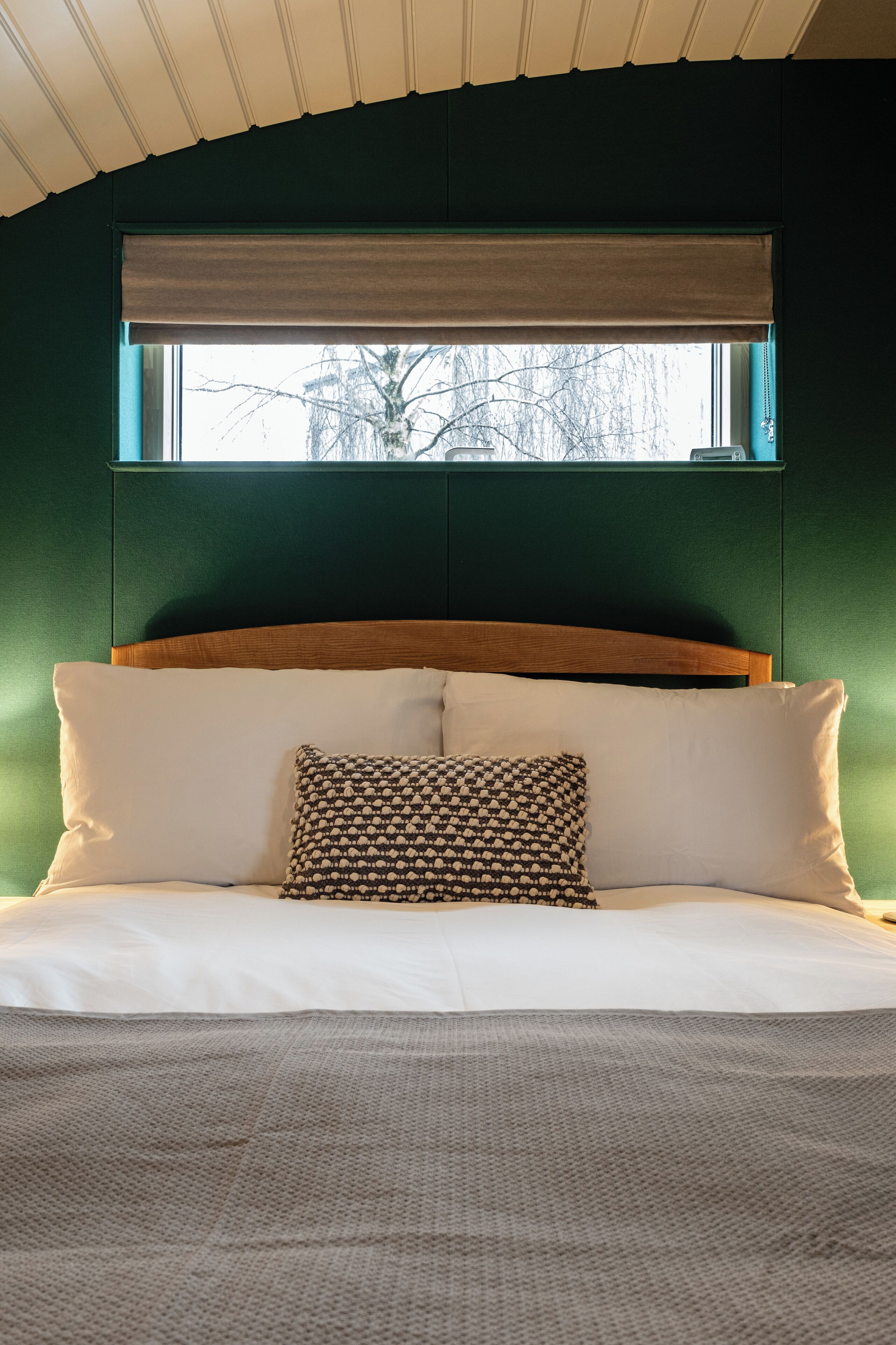 A bedroom with a bed, a patterned pillow, and a window with a view of trees.