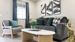 Ein modernes Wohnzimmer mit einem grauen Sofa, einem Holzstuhl, einem runden Couchtisch und einem dekorativen, goldenen Pfau.