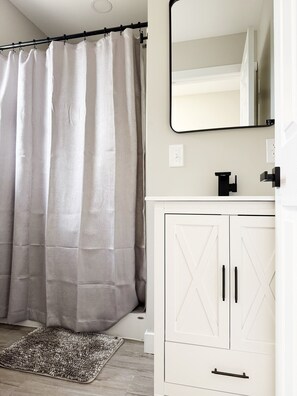 Une salle de bain avec un rideau de douche, un miroir, un lavabo et un meuble de rangement.