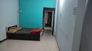 A small, narrow room with a single bed, a wardrobe, and a door leading to another room.