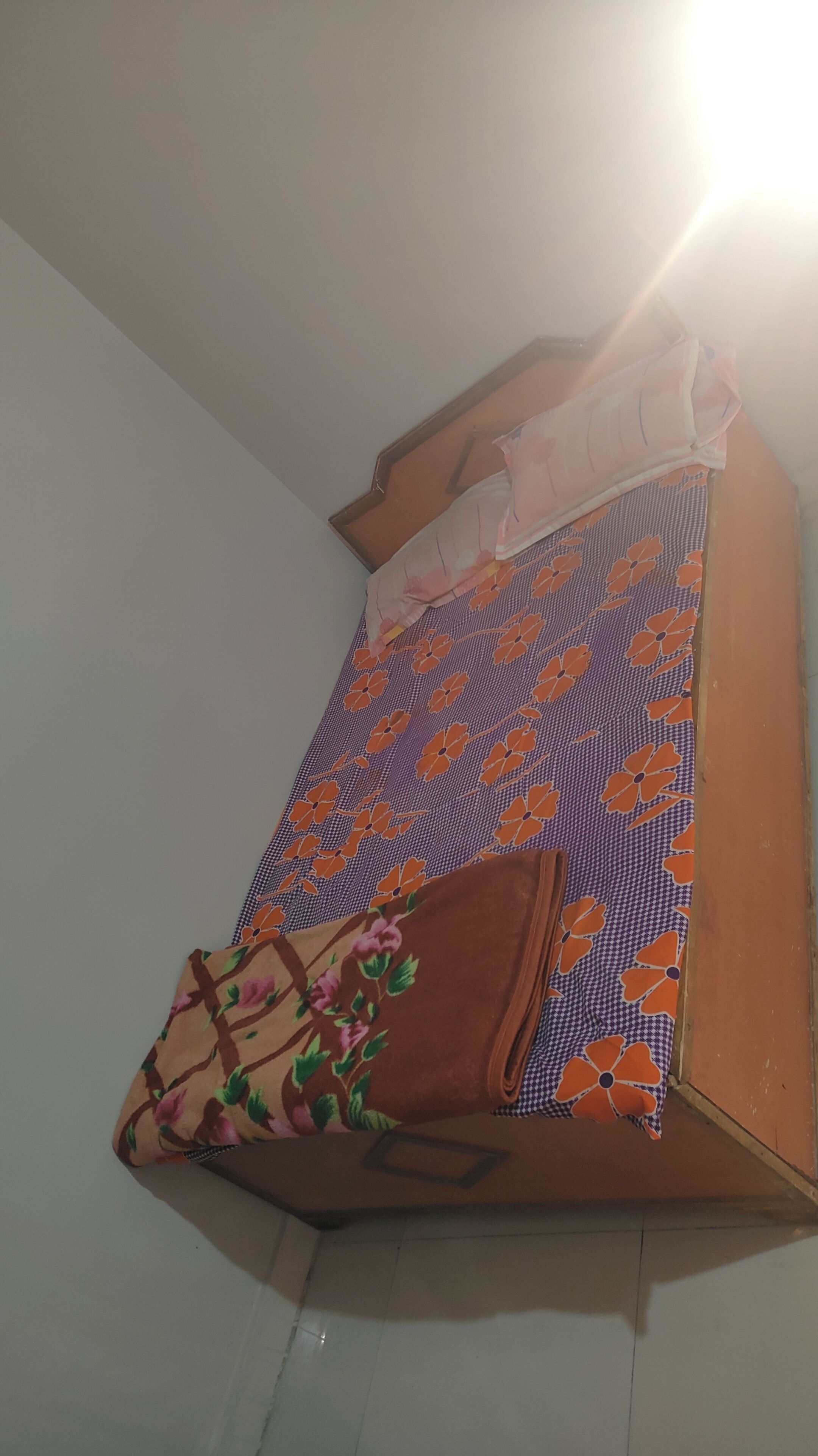 Een hoek van een kamer met een bed, gedekt met een bloemenprintdeken en een bruine deken.