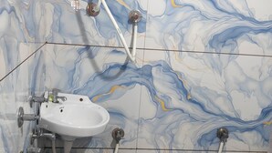 A bathroom with a marble wall design, a white sink, a toilet, and a shower unit with a hose.