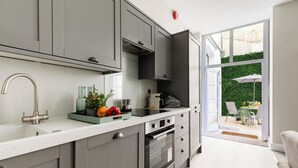 Een moderne keuken met grijze kastjes, een roestvrijstalen spoelbak en een oven. Er is een raam dat uitkomt op een balkon met een tafel en stoelen.