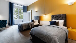 Een hotelkamer met twee bedden, een blauwe fauteuil, een tafeltje en een raam met gordijnen.