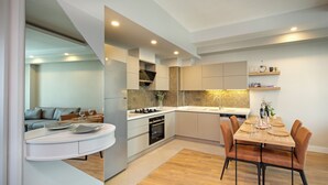 A modern kitchen with white cabinetry, a wooden dining table, and a built-in oven.