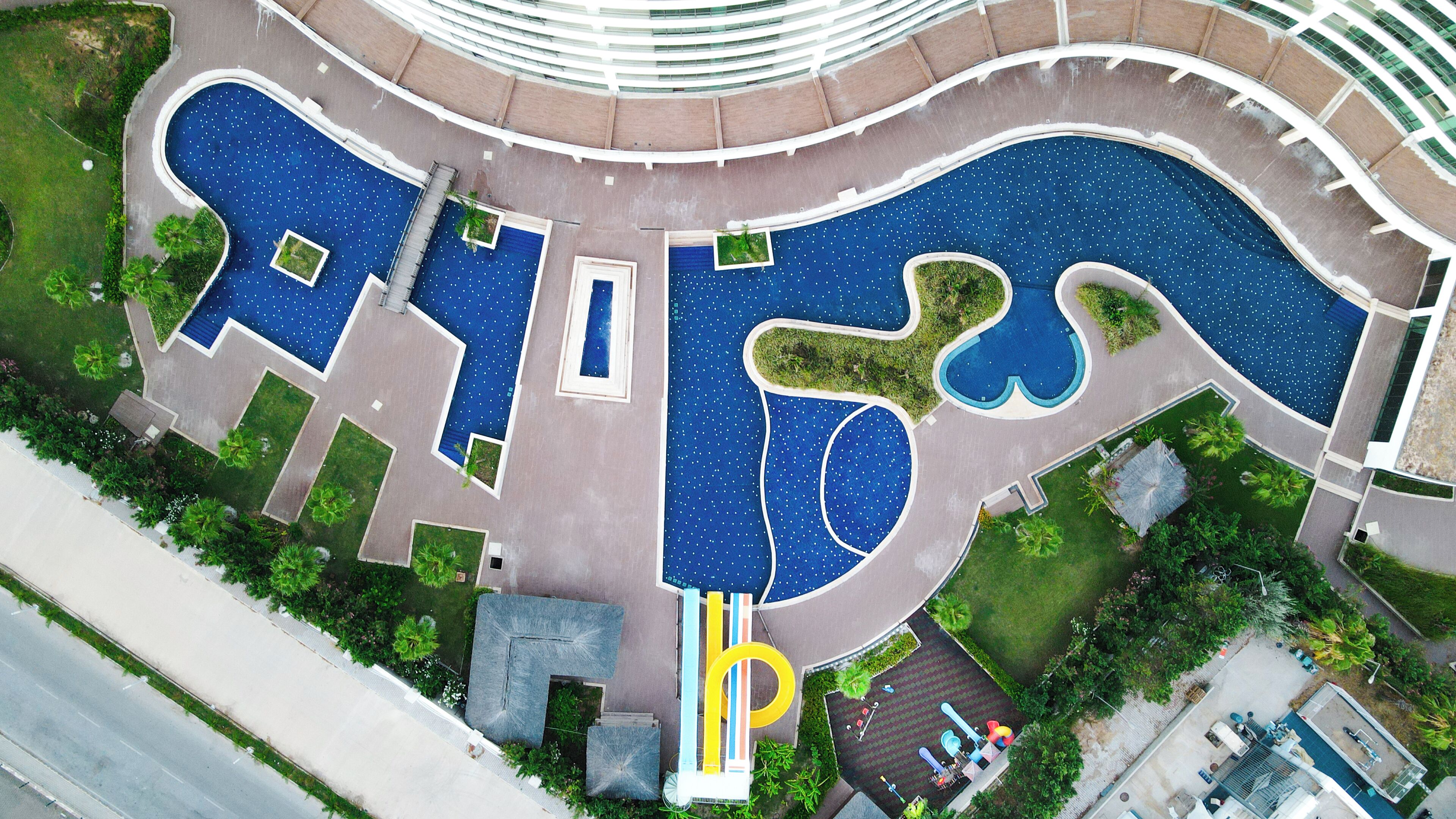 Vista aérea de un hotel moderno con una piscina central, varias piscinas más pequeñas y una estructura de edificio circular.