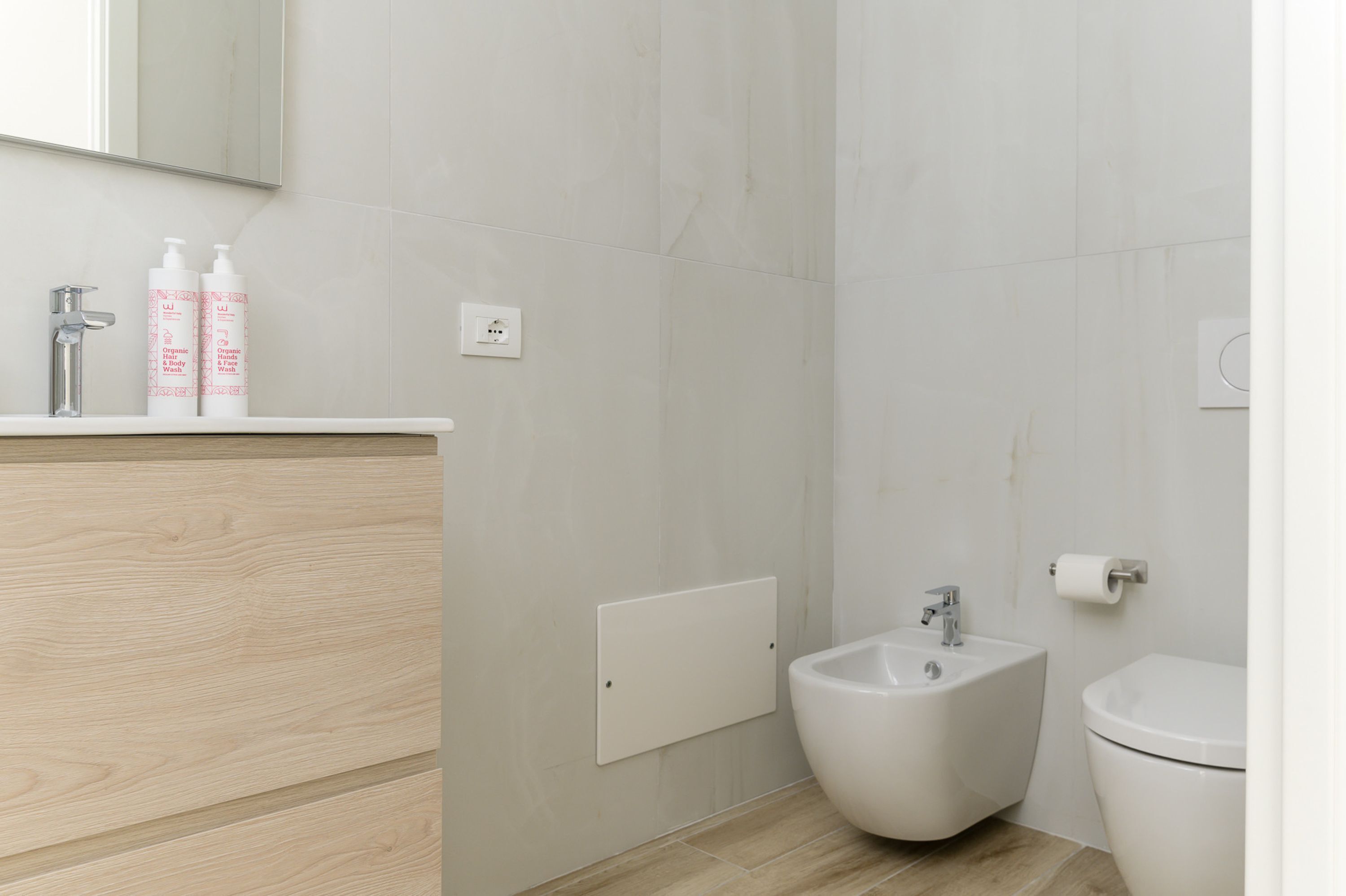 A modern bathroom with a wooden vanity, a bidet, and a toilet.