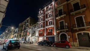 Vista nocturna de una calle con edificios de varios pisos, coches aparcados y un local comercial a la vista.