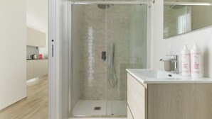 Un baño moderno con ducha de vidrio, lavamanos con espejo y artículos de aseo en la encimera.