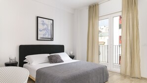 A bedroom with a large bed, a nightstand, a bedside table, a framed picture on the wall, and a view of the outside balcony. - Palazzo Murat - Apartment With City View by Wonderful Italy (Bari)