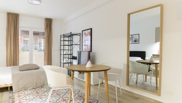 Ein Hotelzimmer mit einem Bett, einem runden Tisch mit Stühlen, einem großen Spiegel und einem Fenster mit Vorhängen.