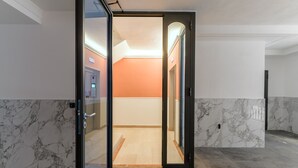 Eine moderne Hotelhalle mit Marmorboden, einem Glastür-Eingang und Blick in einen hell erleuchteten Raum mit orangefarbenen Wänden.