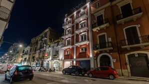 Nachts beleuchtete Strassenansicht mit mehrstöckigen Gebäuden, parkenden Autos und Strassenlaternen.