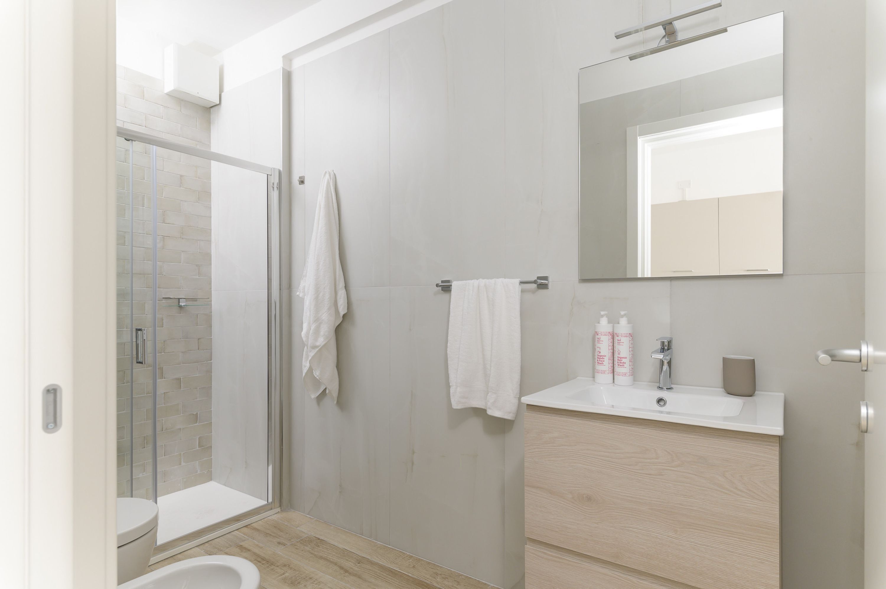 A modern bathroom with a glass shower enclosure, a white sink, and a large mirror.