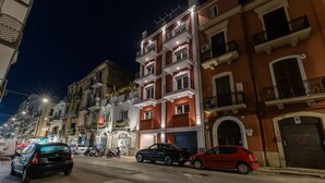 A street view at night with multi-story buildings, parked cars, and a visible storefront. - Palazzo Murat - One-bedroom Apartment With Terrace by Wonderful Italy (Bari)