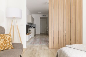 A modern hotel room with a bed, a sofa, a floor lamp, and a kitchen area in the background. - Palazzo Murat - One-bedroom Apartment With Balcony by Wonderful Italy (Bari)