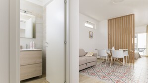 A modern living room with a sofa, a dining table with chairs, a wooden partition, and a large window. - Palazzo Murat - One-bedroom Apartment With Balcony by Wonderful Italy (Bari)