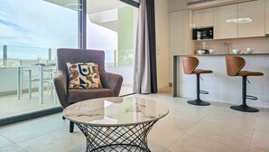Un salon moderne avec une table en verre, un fauteuil marron et deux tabourets de bar.