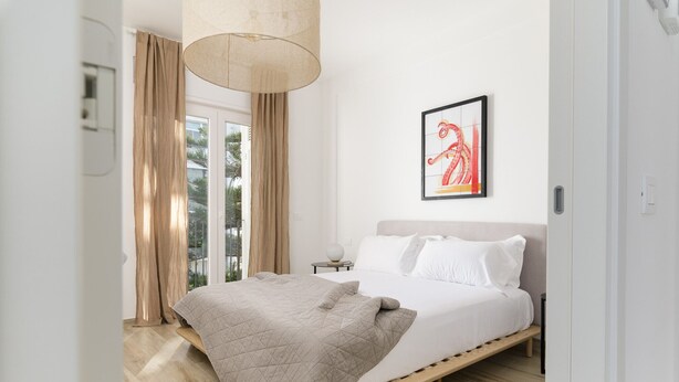 A modern bedroom with a bed, a bedside table, a lamp, and a window with curtains.