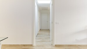 A hallway with a skylight, white walls, and a wooden floor.