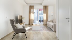 A modern living room with a sofa, armchair, and coffee table, a TV, and a balcony with curtains.
