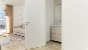 A modern, minimalist room with a beige sofa, a patterned rug, a white door, and a bathroom with a mirror and sink.