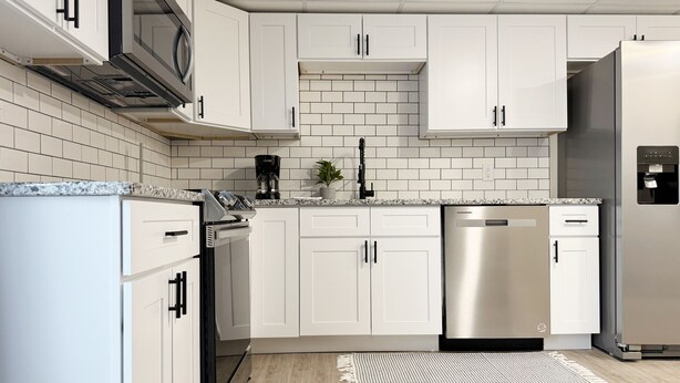 A modern kitchen with white cabinets, stainless steel appliances, and a tiled backsplash. - RiverStone Retreat C (Newburgh)