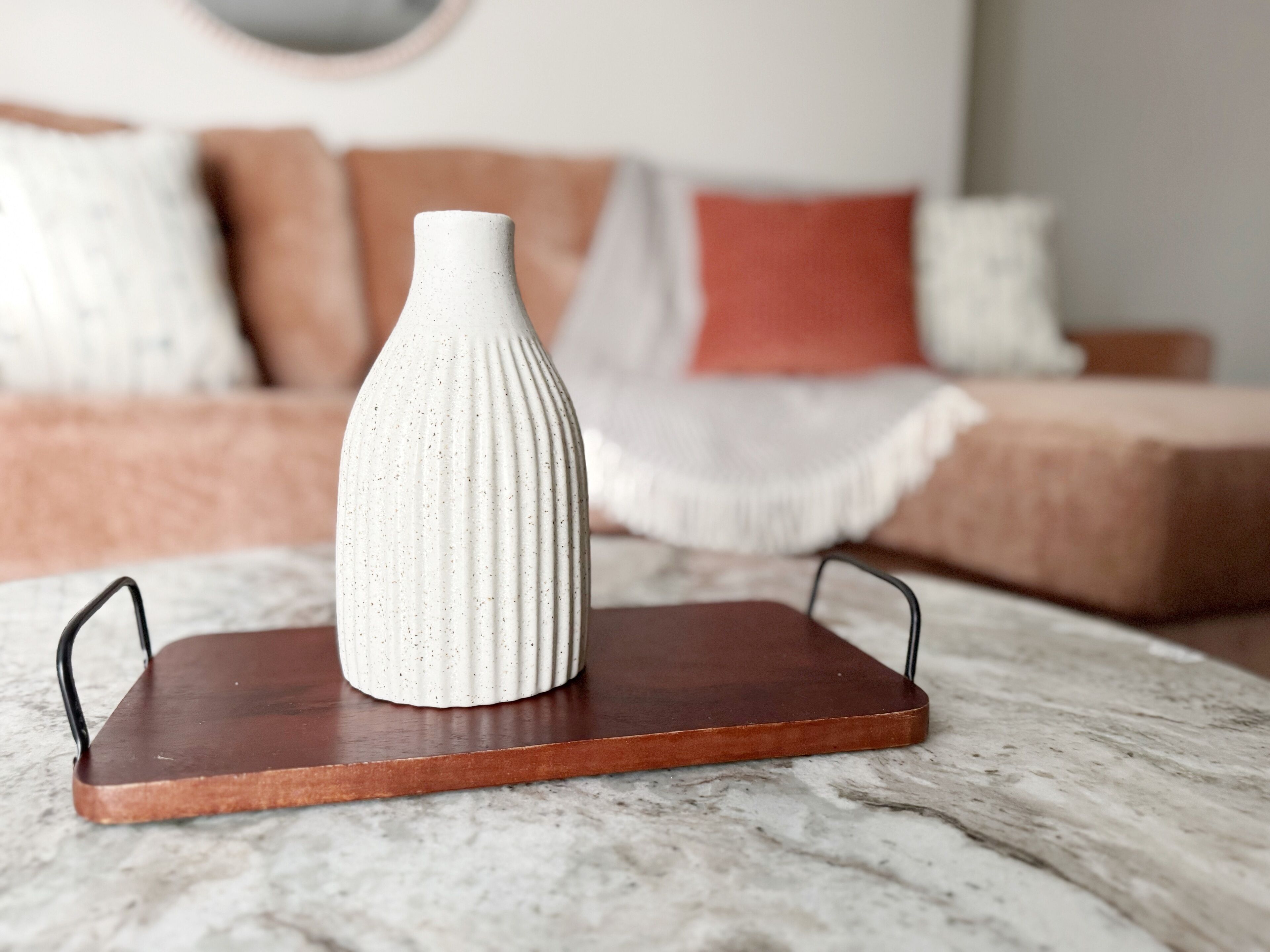 Un florero blanco sobre un posavasos de madera sobre una mesa de mármol.